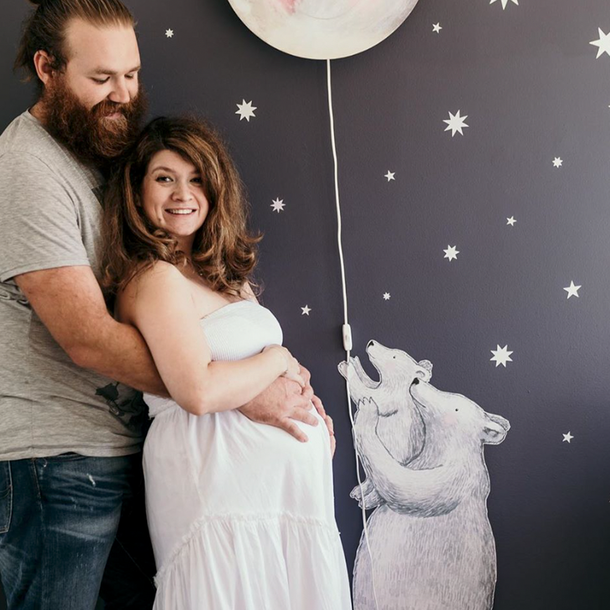 Aanstaande ouders in babykamer met Hartendief berenmuursticker, witte sterrenstickers en maanlamp