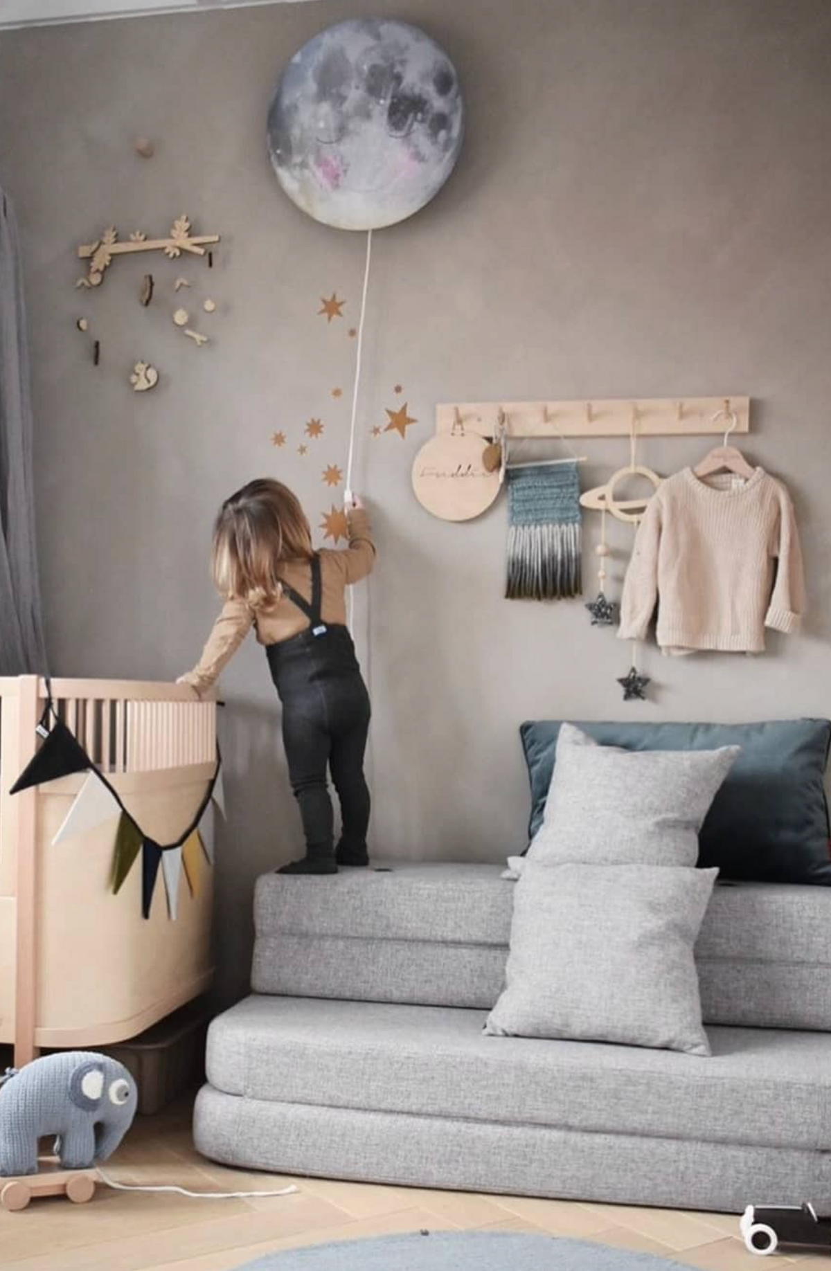 Toddler reaching up to the Sleepy Moon wall lamp by Hartendief on a taupe wall with golden stars