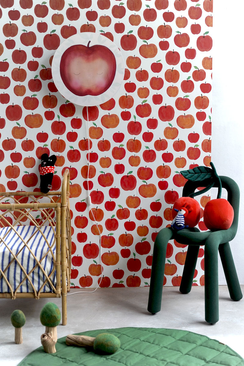Close-up of the Funky Apples nursery wallpaper by Hartendief with a green chair, cherry cushion and cot