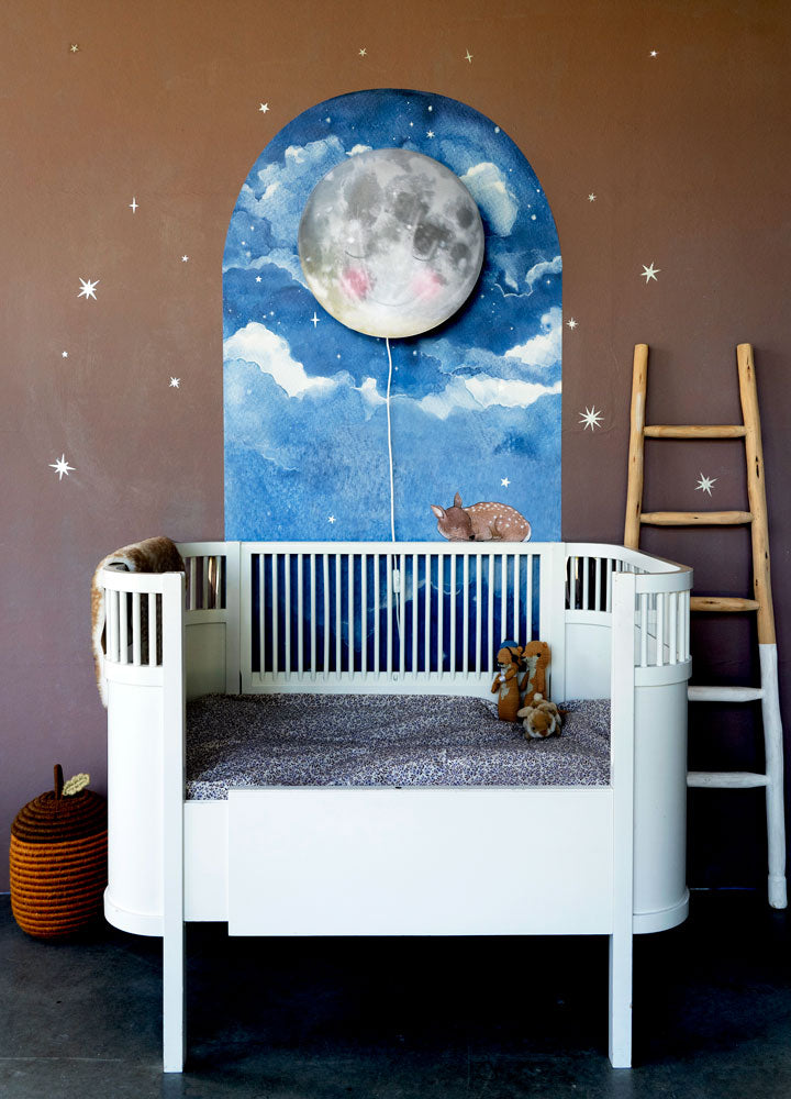 In de Wolken behangboog van Hartendief op een caramelkleurige muur met wit kinderbedje en de Ga Slapen Maan wandlamp