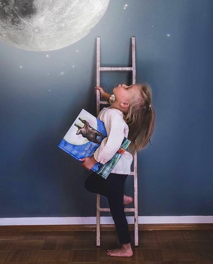Mädchen auf einer kleinen Leiter gibt dem Mond einen Kuss, mit dem Hartendief-Bilderbuch unter dem Arm