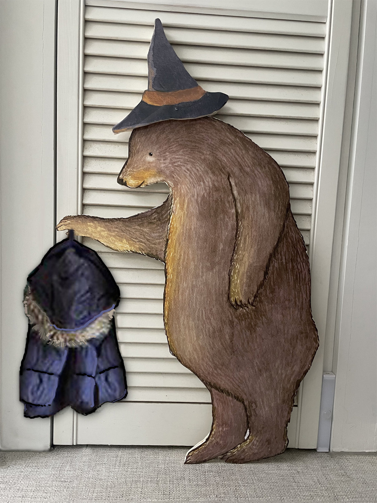 Night Bear with witch's hat against a white louvred door, with a child's jacket on a hook at his paw – Hartendief wall decal as a coat hook